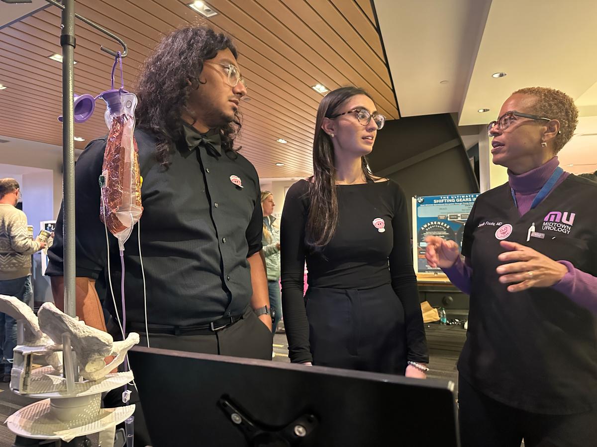 Three people talking in front of an IV bag filled with liquid
