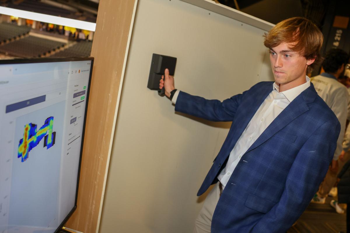 man holds device against a wall while computer screen shows imaging