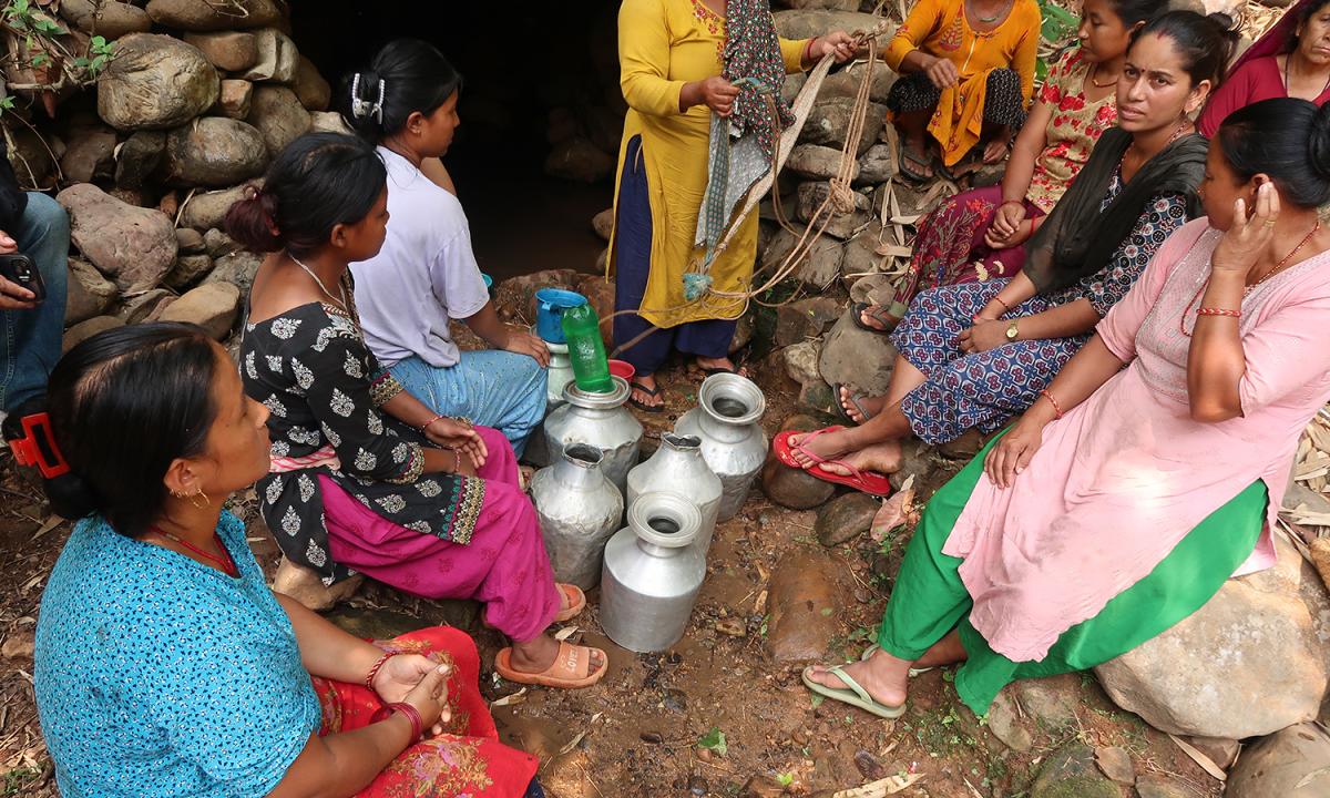 Women gather with aluminum containers at a water source in Nepal.
