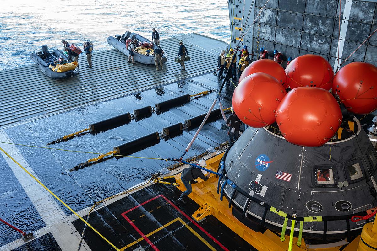 boats of people and a model of the Orion capsule perform recovery training at sea