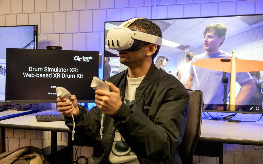 a student wears a VR headset and two handheld controllers with a screen in the background