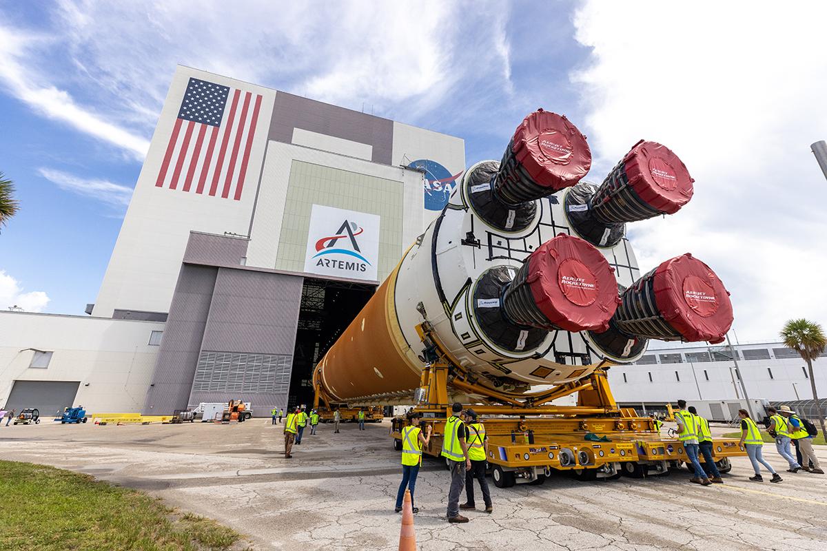 The Space Launch System is loaded into NASA's Vehicular Assembly Building, with many crew members around it