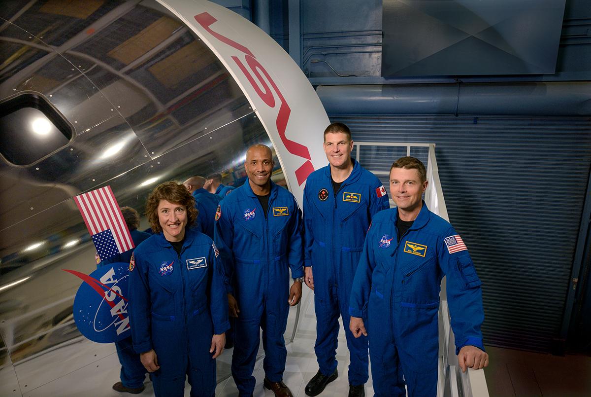 four astronauts stands in front of a spacecraft simulator