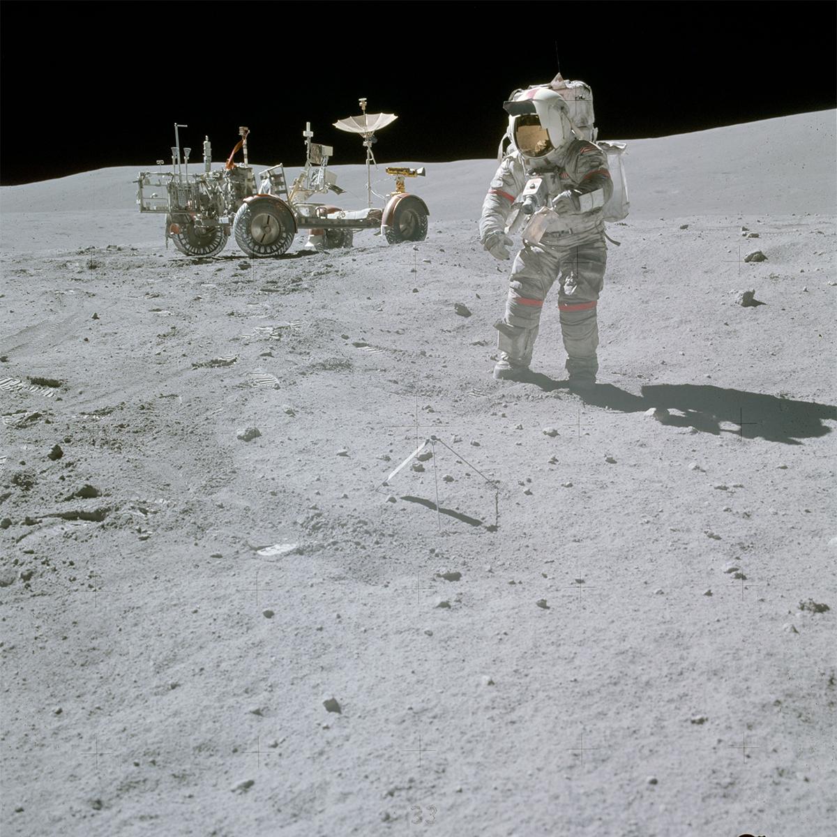 Astronaut John Young collects lunar samples with a lunar rover in the background
