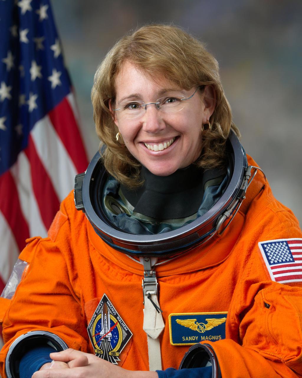 Sandra Magnus in an astronaut suit with the American flag in the background