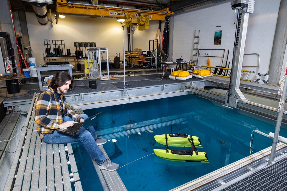 a person sits on the edge of a water tank monitoring a small watercraft on the surface