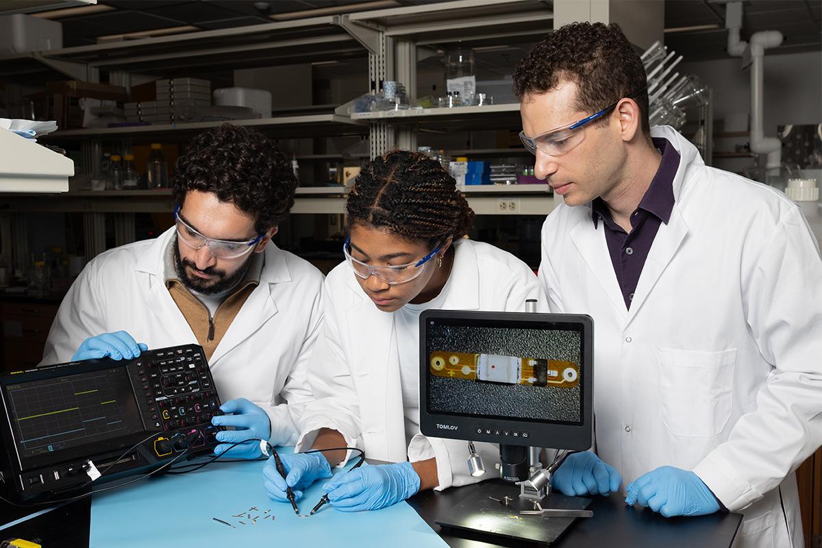 three people in lab coats look at device data on a screen
