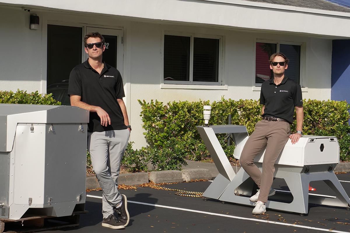 Two people stand outdoors with drone docking stations