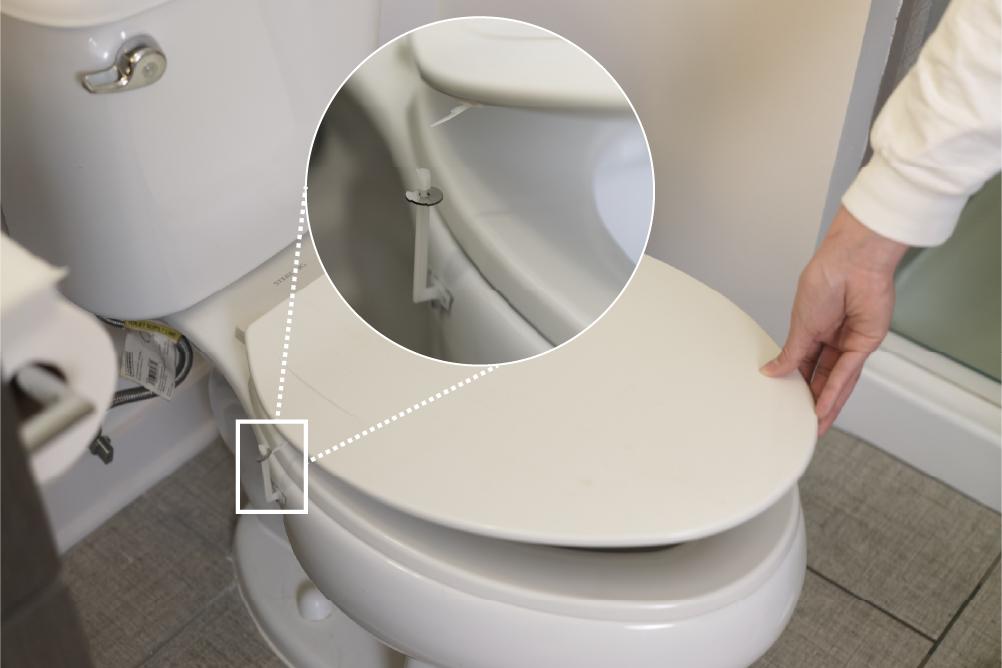 A person lifting the lid of a toilet. An inset shows a prototype metal ultrasonic tag attached to the lid and bowl that is activated upon opening.