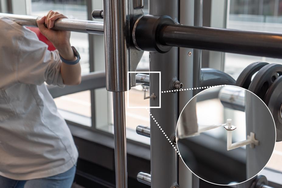 A person doing squats in the gym with a prototype metal ultrasonic tag attached to the machine to count reps.