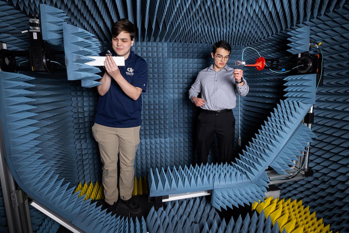 Two people work with antennae in a chamber with acoustic walls
