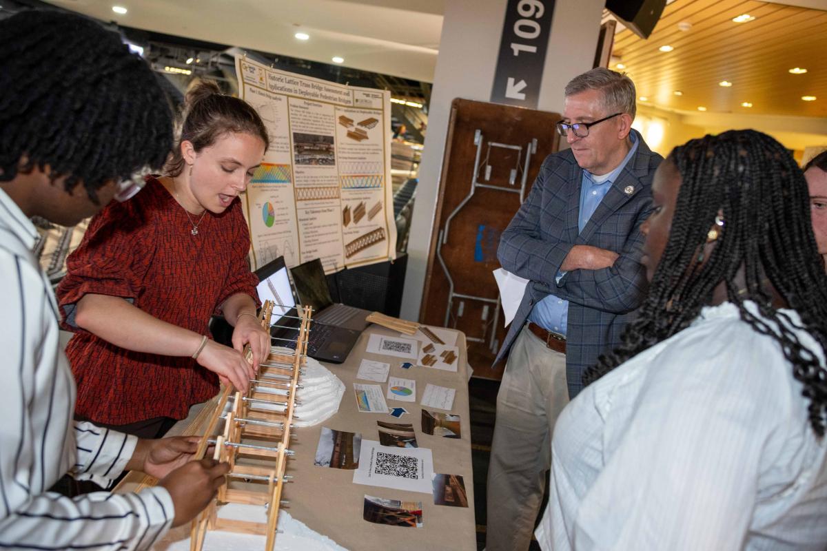 people looking at two students showing a model of a bridge