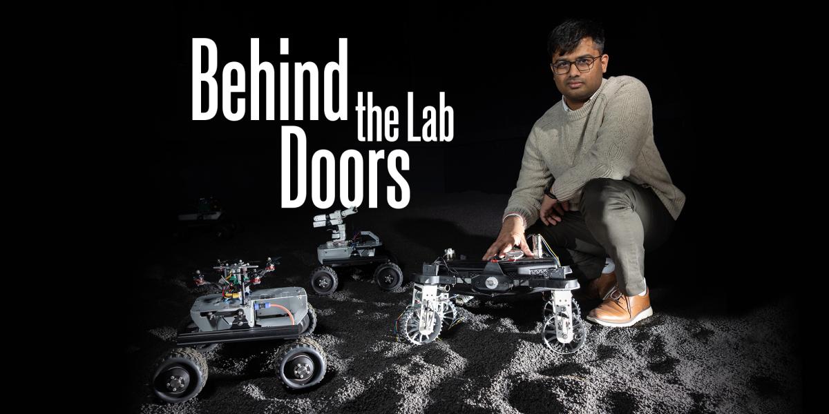 a person kneels with robots on a gravelly surface against a black background. Title text overlay reads "Behind the Lab Doors"