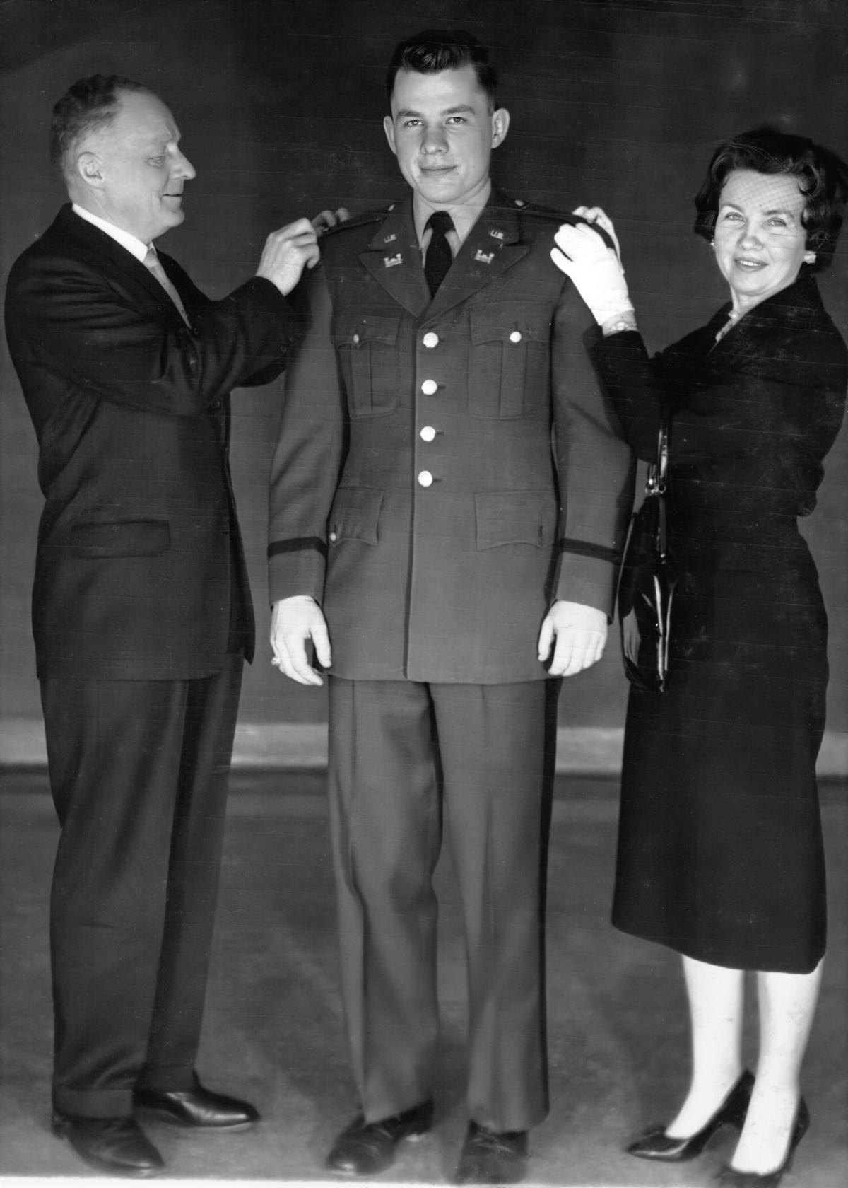 A young Ken Grundborg stands in uniform with his mother and father attaching new rank insignia on each shoulder.
