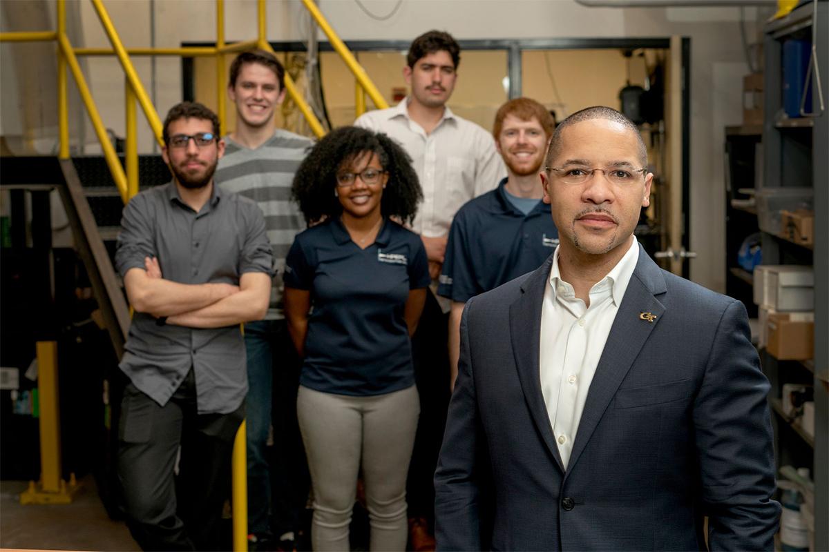 A group of people stand in a lab behind one person in the foreground