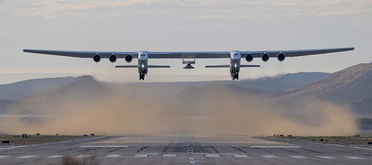 a large airplane carrying a hypersonic craft takes off from a runway in the desert