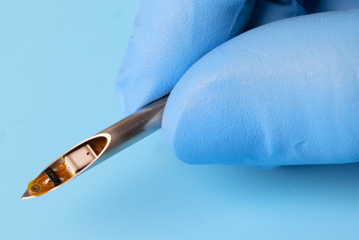Two fingers holding a syringe needle that has a small implant positioned inside.
