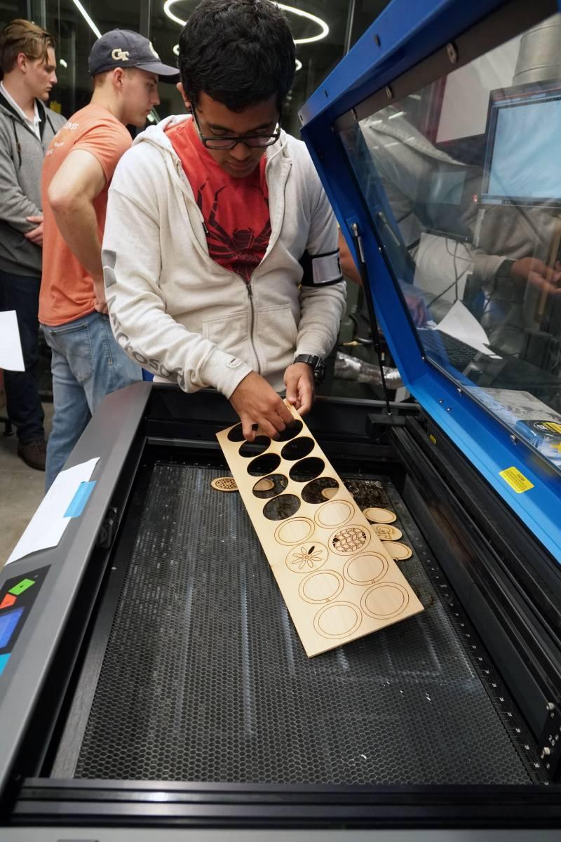 A student works on a project at a laser cutting machine.