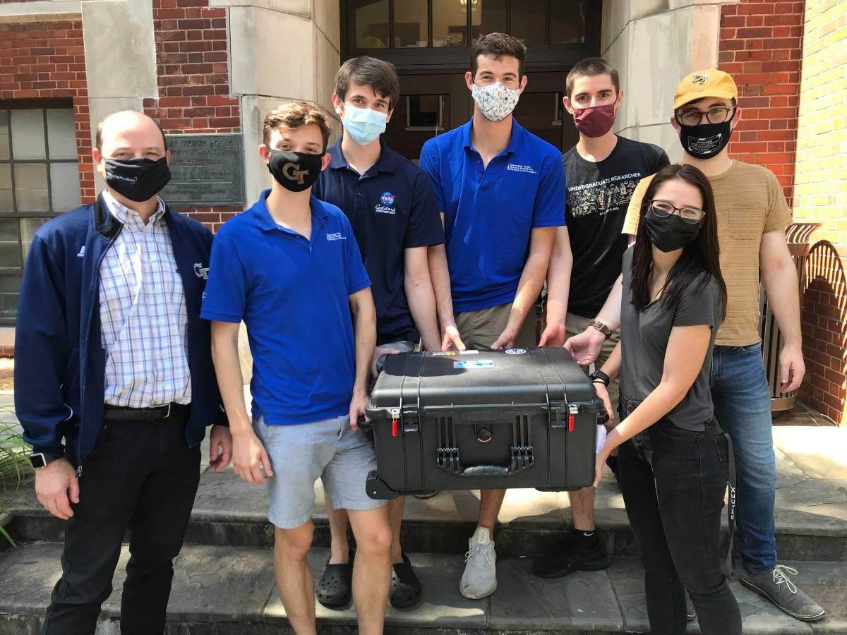 team members carrying satellite in a box