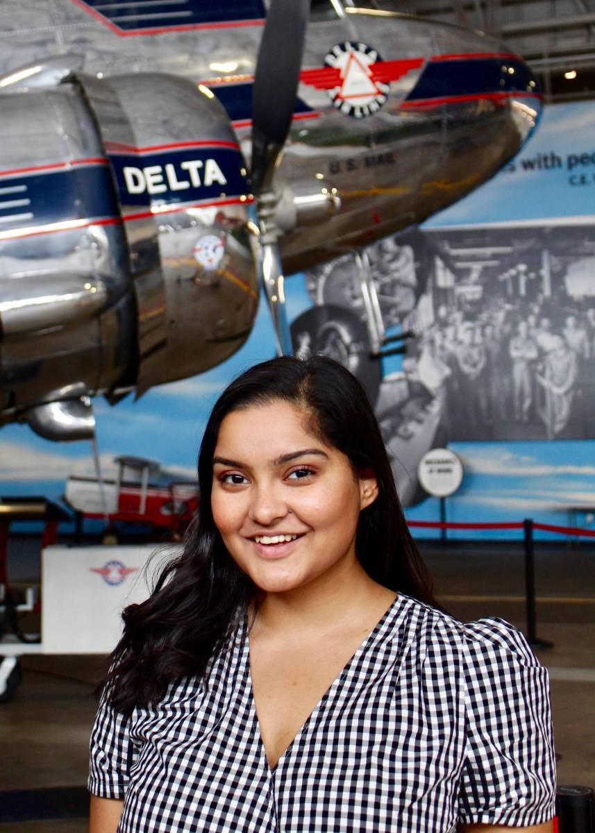 Rikhi Roy standing in front of a Delta plane exhibit
