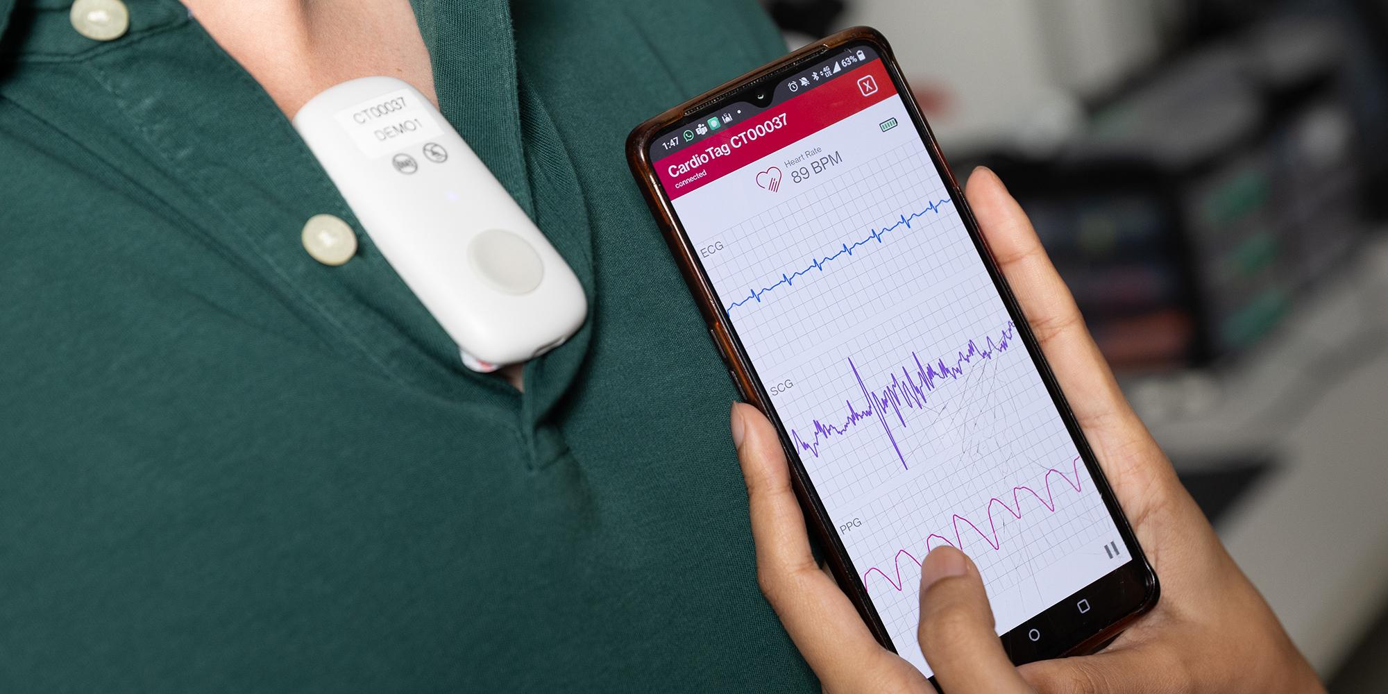 A smartphone displays heart monitoring data from a CardioTag device worn by Ph.D. student Onur Selim Kilic.